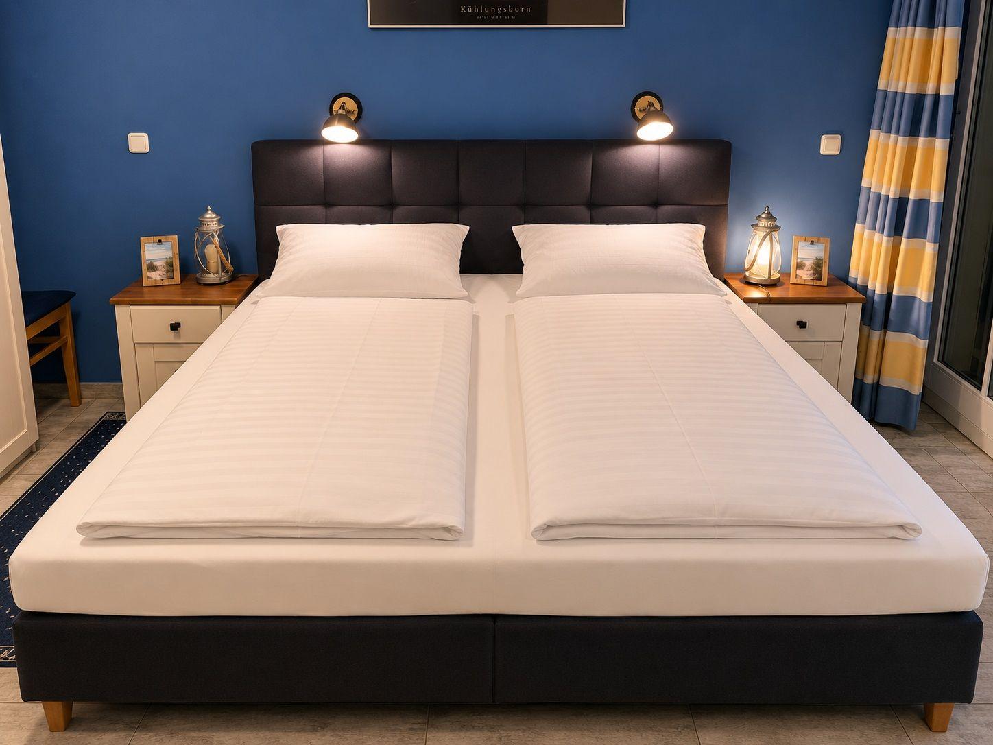 Doppelbett mit weißen Bettwäsche, zwei Nachttische und blaue Wand.