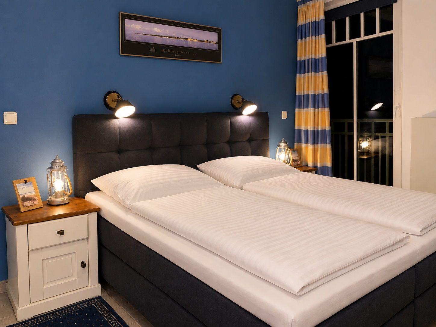 Schlafzimmer mit Doppelbett, Nachttisch und Fenster mit Vorhängen.