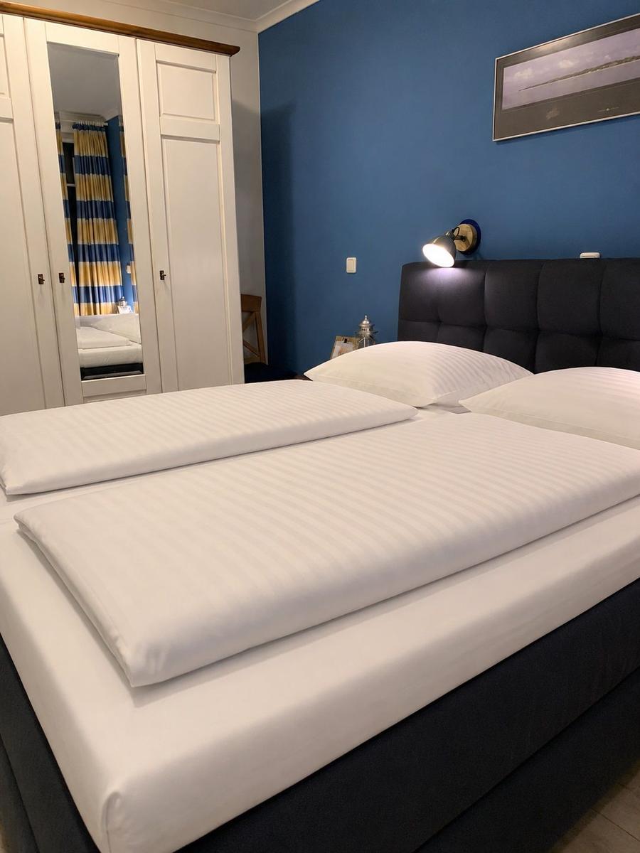 Schlafzimmer mit Doppelbett, blauer Wand und Kleiderschrank mit Spiegel.