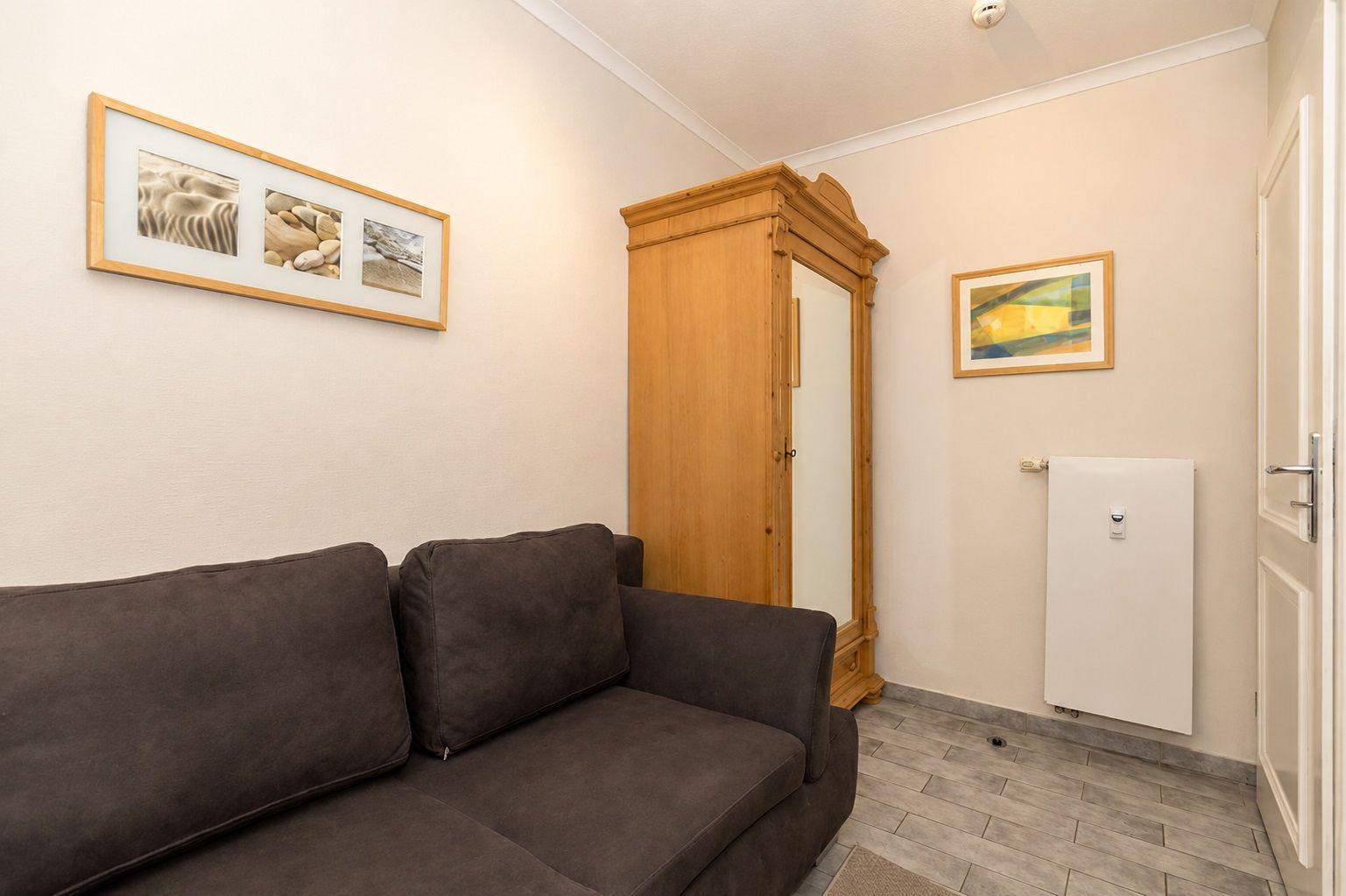 Ein Raum mit braunem Sofa, Holzschrank und Wandbildern.