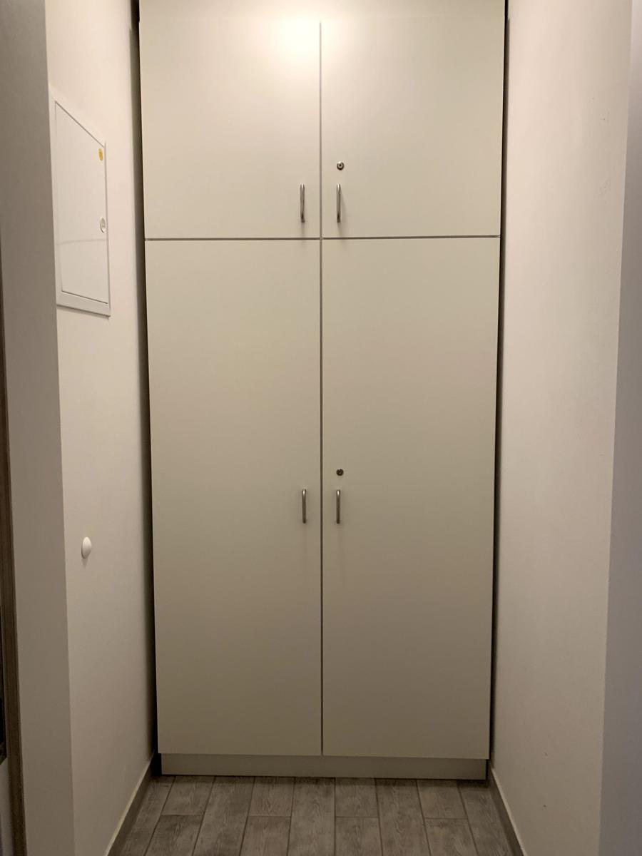 Weißer Schrank mit vier Türen und Metallgriffen in einem Flur mit Holzdielen.