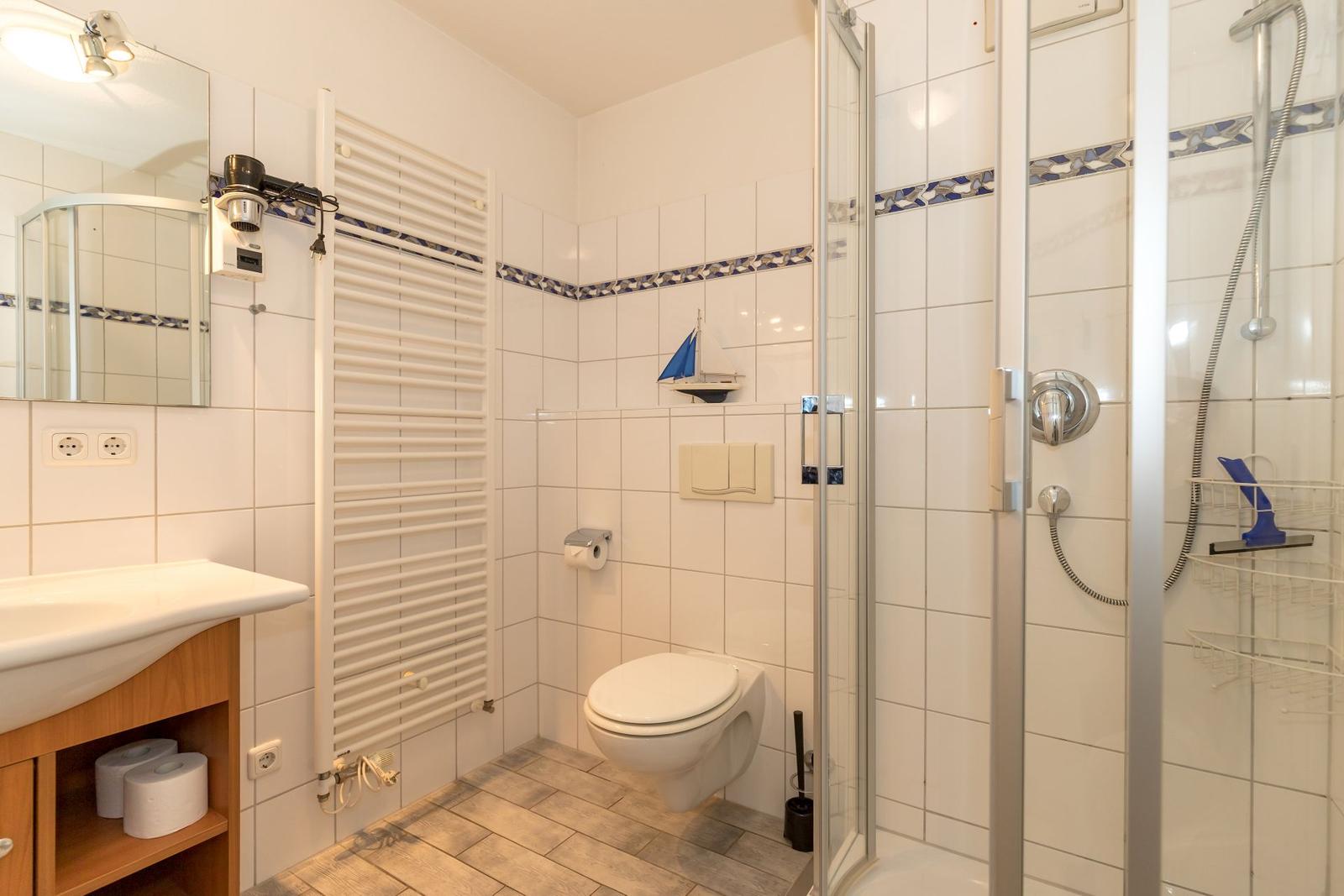 Badezimmer mit Dusche, WC und Waschbecken. Fliesenwand mit blauer Bordüre.