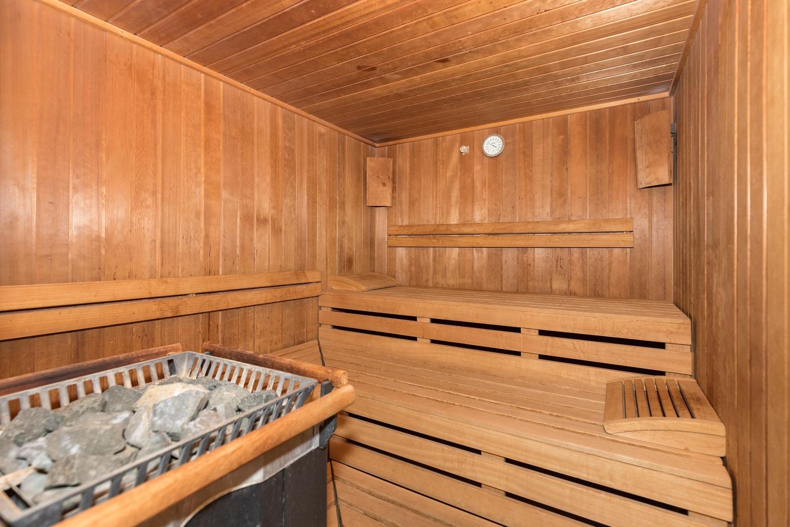 Holzsauna mit Sitzbänken und Steinkorb. Thermometer an der Wand.