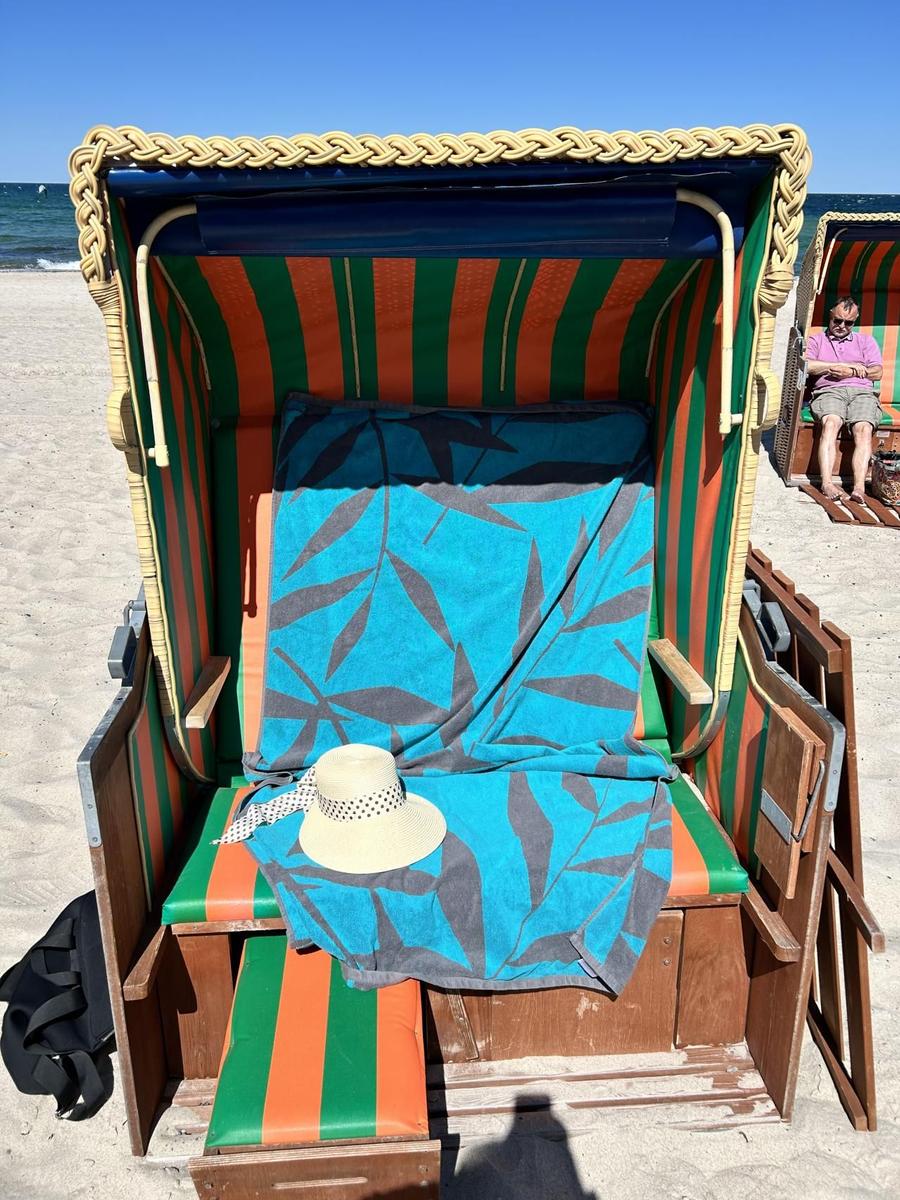 Strandkorb mit blauem Handtuch und Strohhut auf Sand