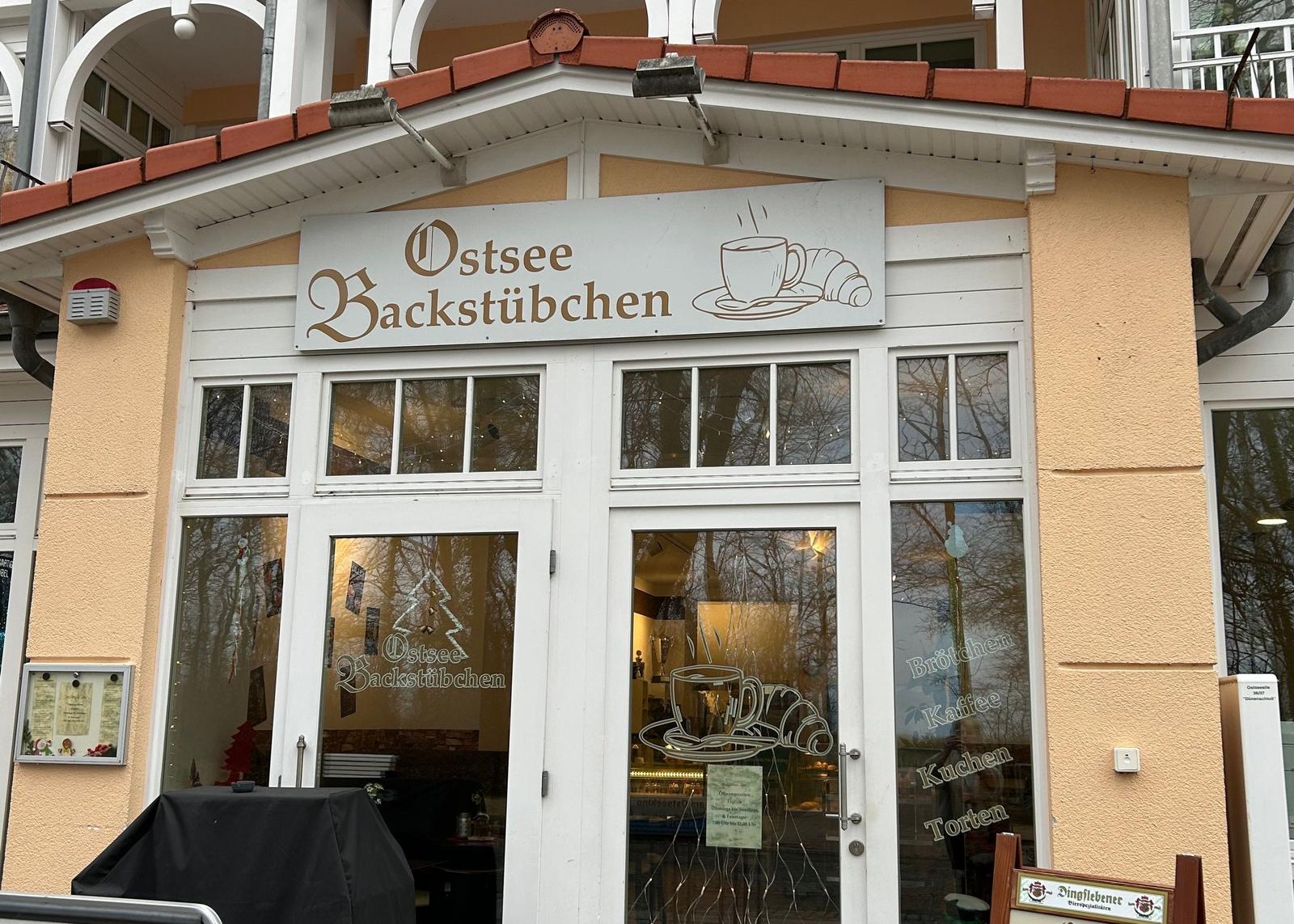 Ostsee Backstübchen mit Glasfront und Schild. Angebot: Brötchen, Kaffee, Kuchen, Torten.