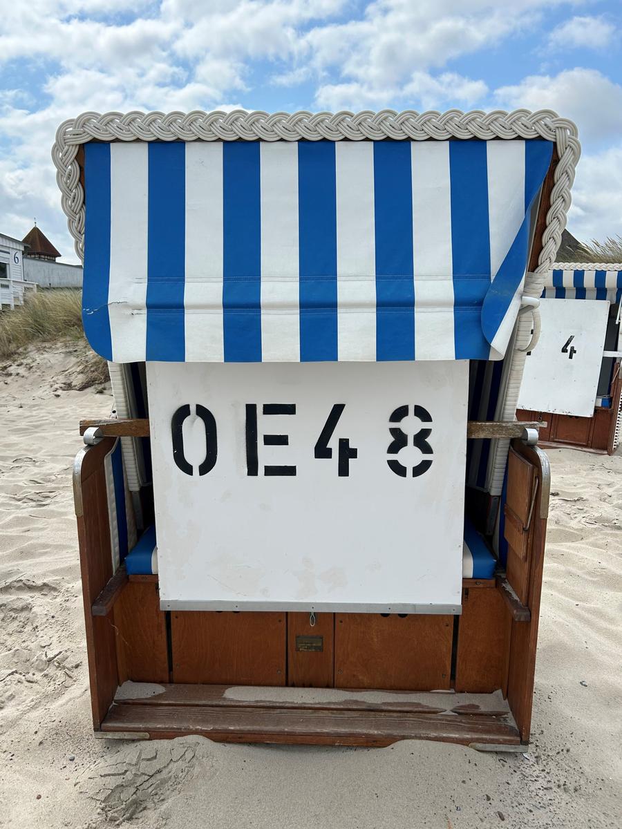 Strandkorb mit blau-weißem Streifenmuster und Kennzeichnung OE48 auf Sand