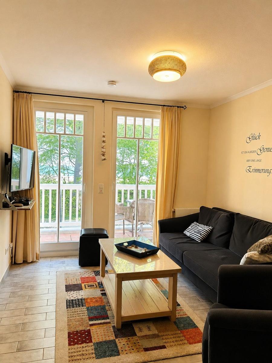 Wohnzimmer mit Sofa, Couchtisch und Balkontür. Fernseher an Wand montiert.