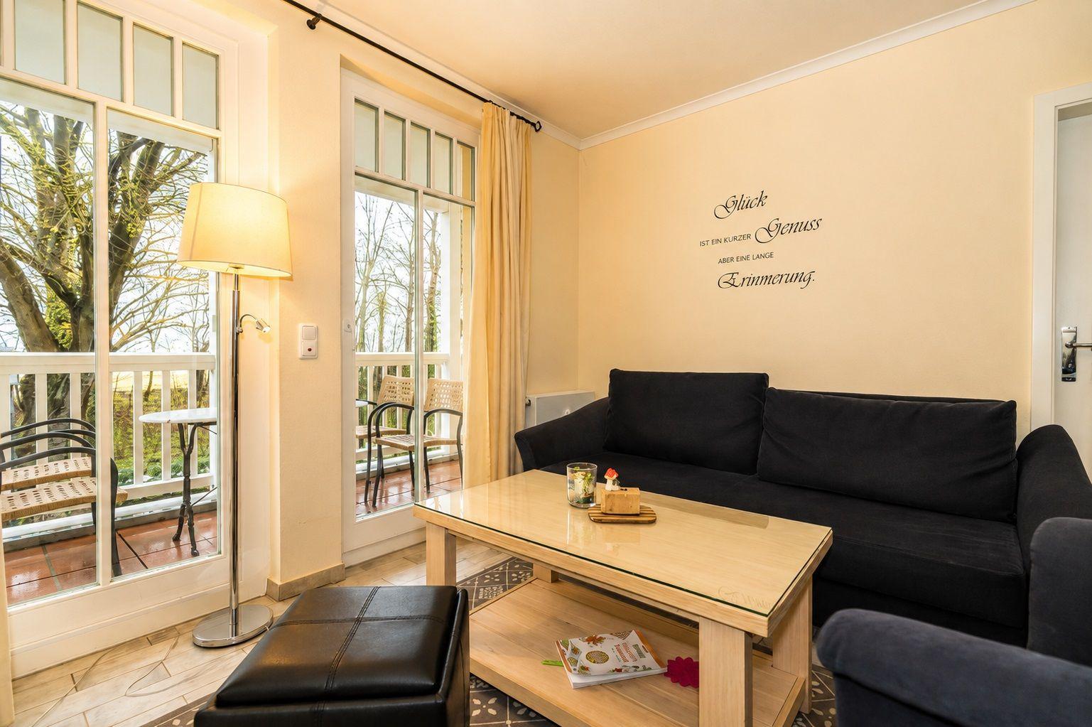Wohnzimmer mit Sofa, Couchtisch und Balkon. Wanddekoration mit Zitat.