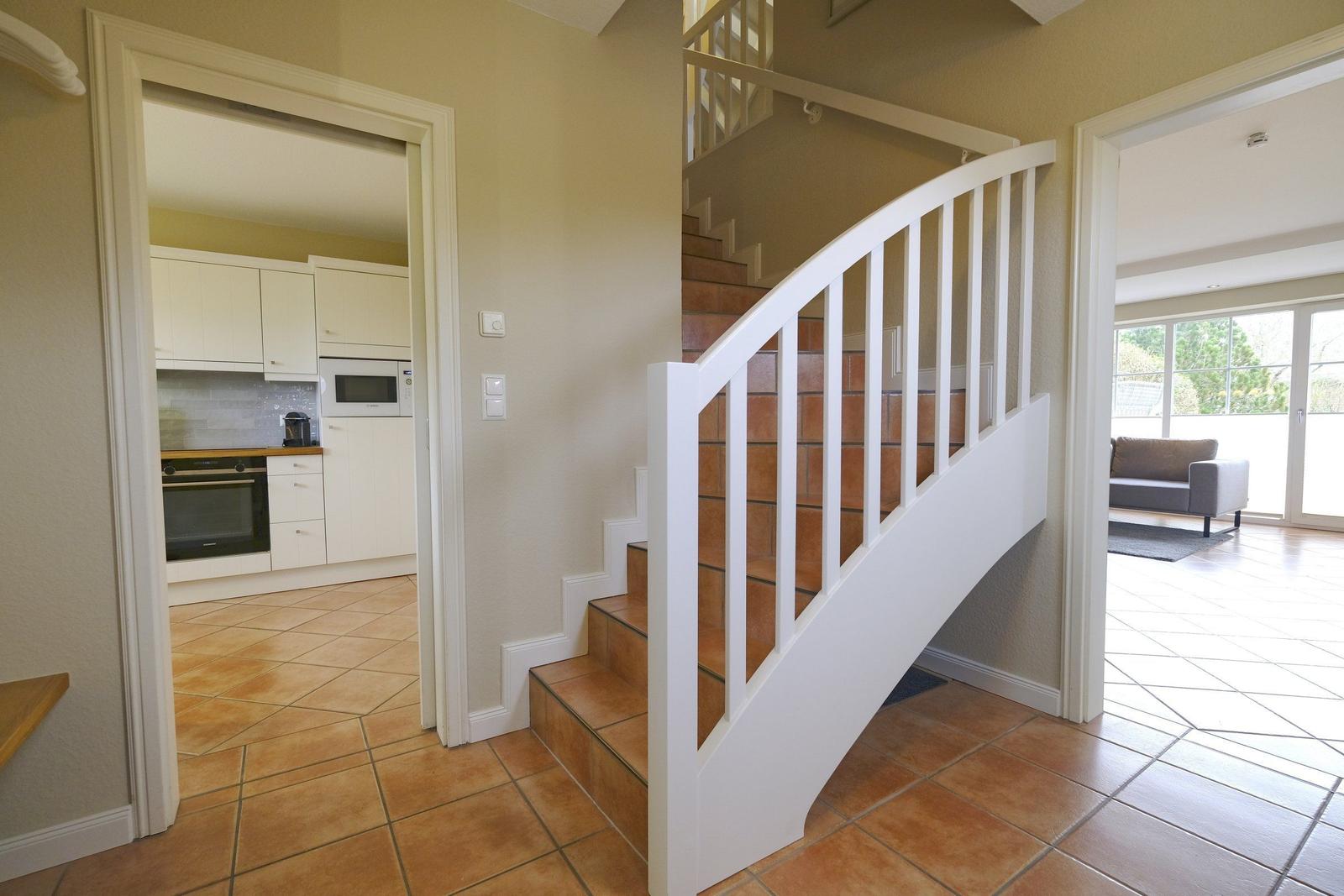 Treppenhaus mit weißer Balustrade, Küche und Wohnzimmer im Hintergrund.