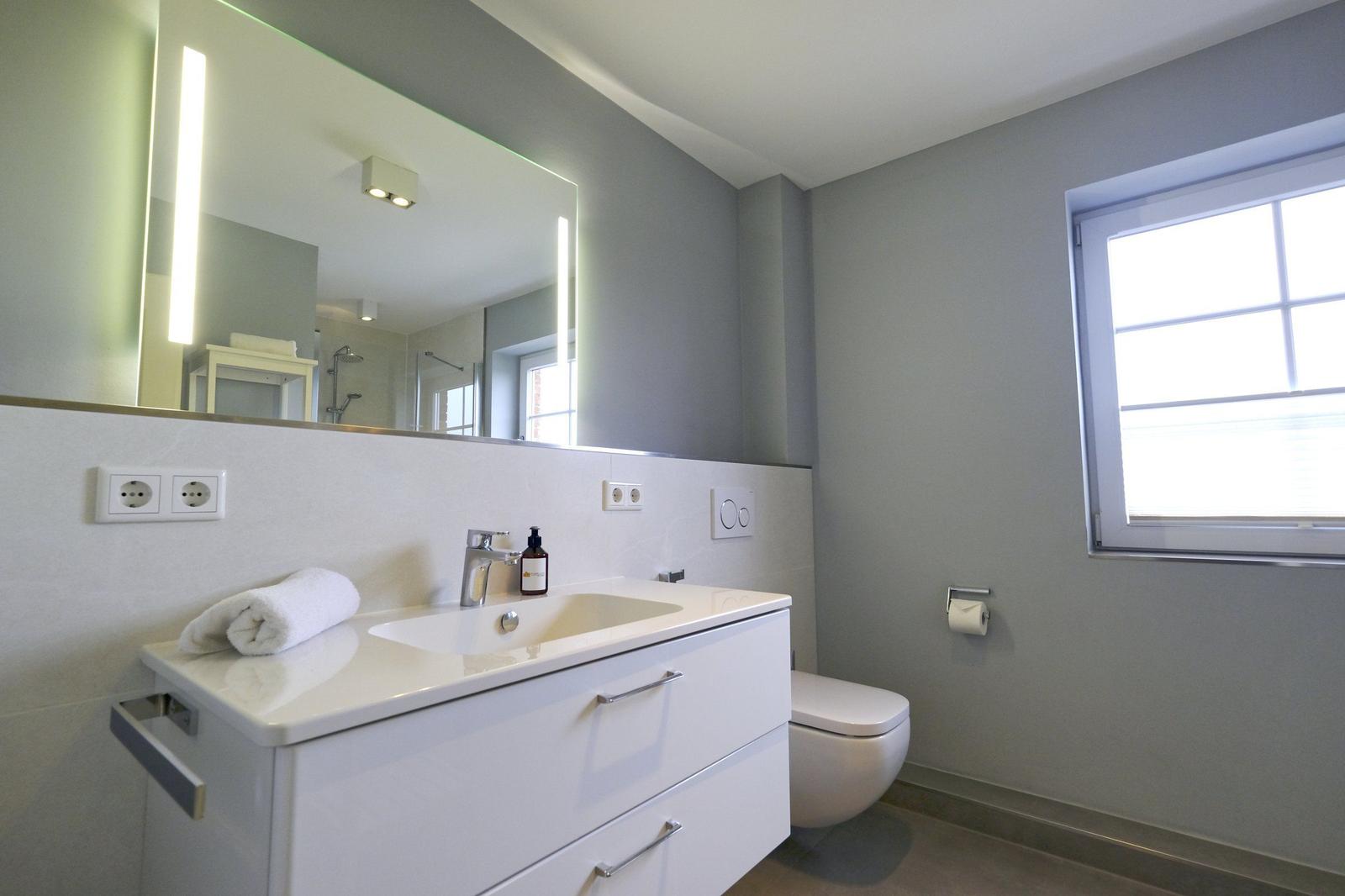 Badezimmer mit Waschbecken, Spiegel, Toilette und Fenster.