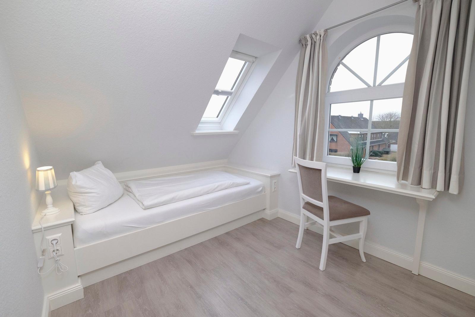 Schlafzimmer mit Dachschrägen, Bett, Schreibtisch und Fenster.