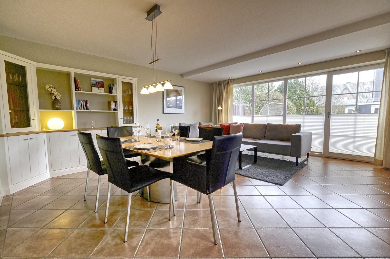 Essbereich mit Tisch und Stühlen, Wohnbereich mit Sofa und Fensterfront.