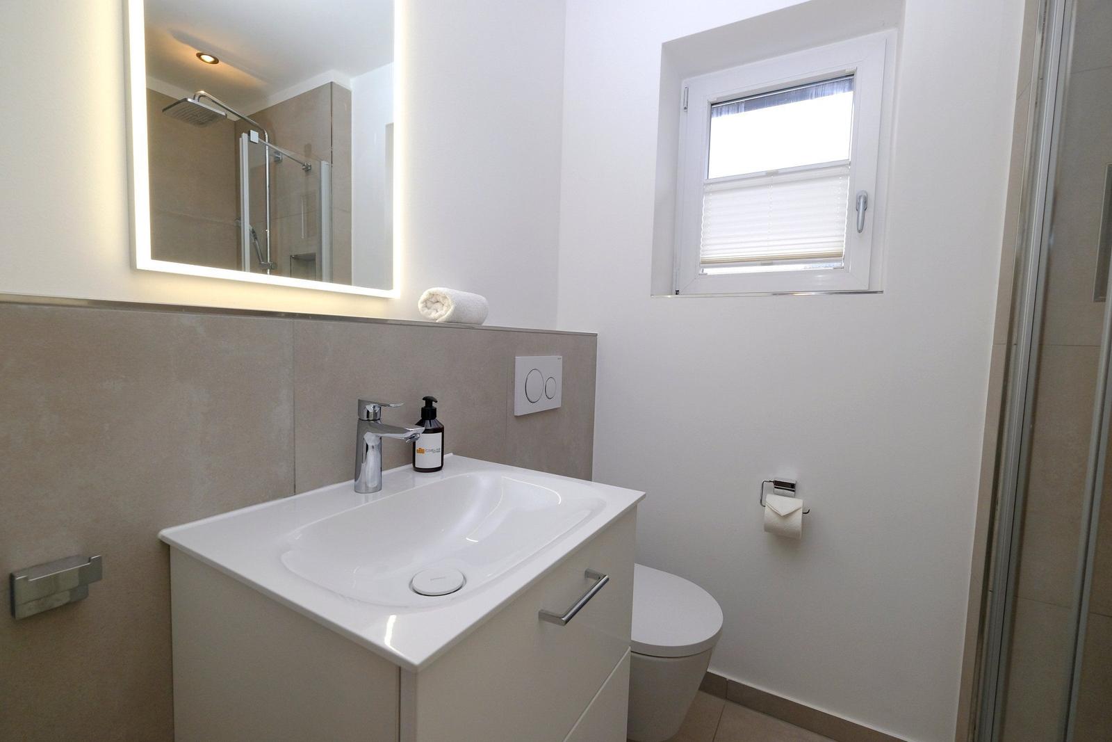 Badezimmer mit Waschbecken, Spiegel, Toilette und Dusche.