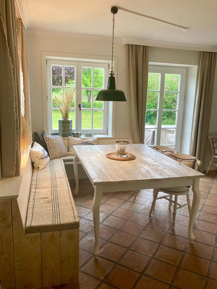 Esszimmer mit Holztisch, Sitzbank und Fenstern zur Grünfläche.