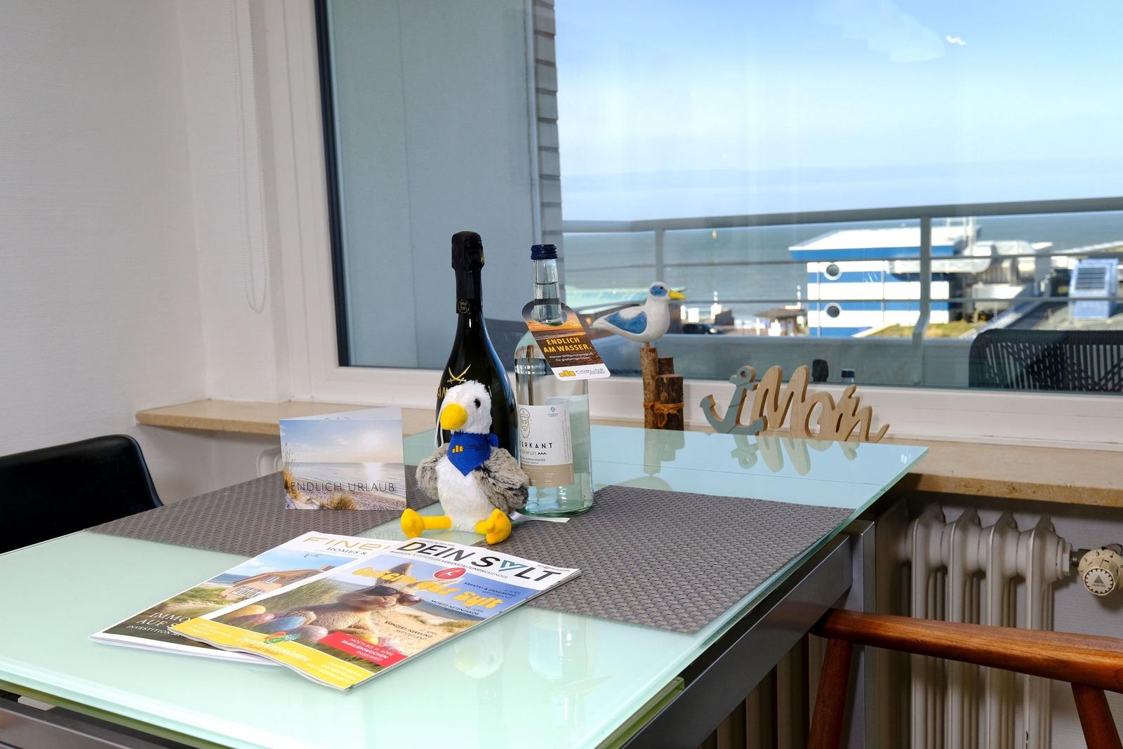 Tisch mit Flaschen, Zeitschriften und Meeresmotiven vor Fenster mit Blick auf Hafen.