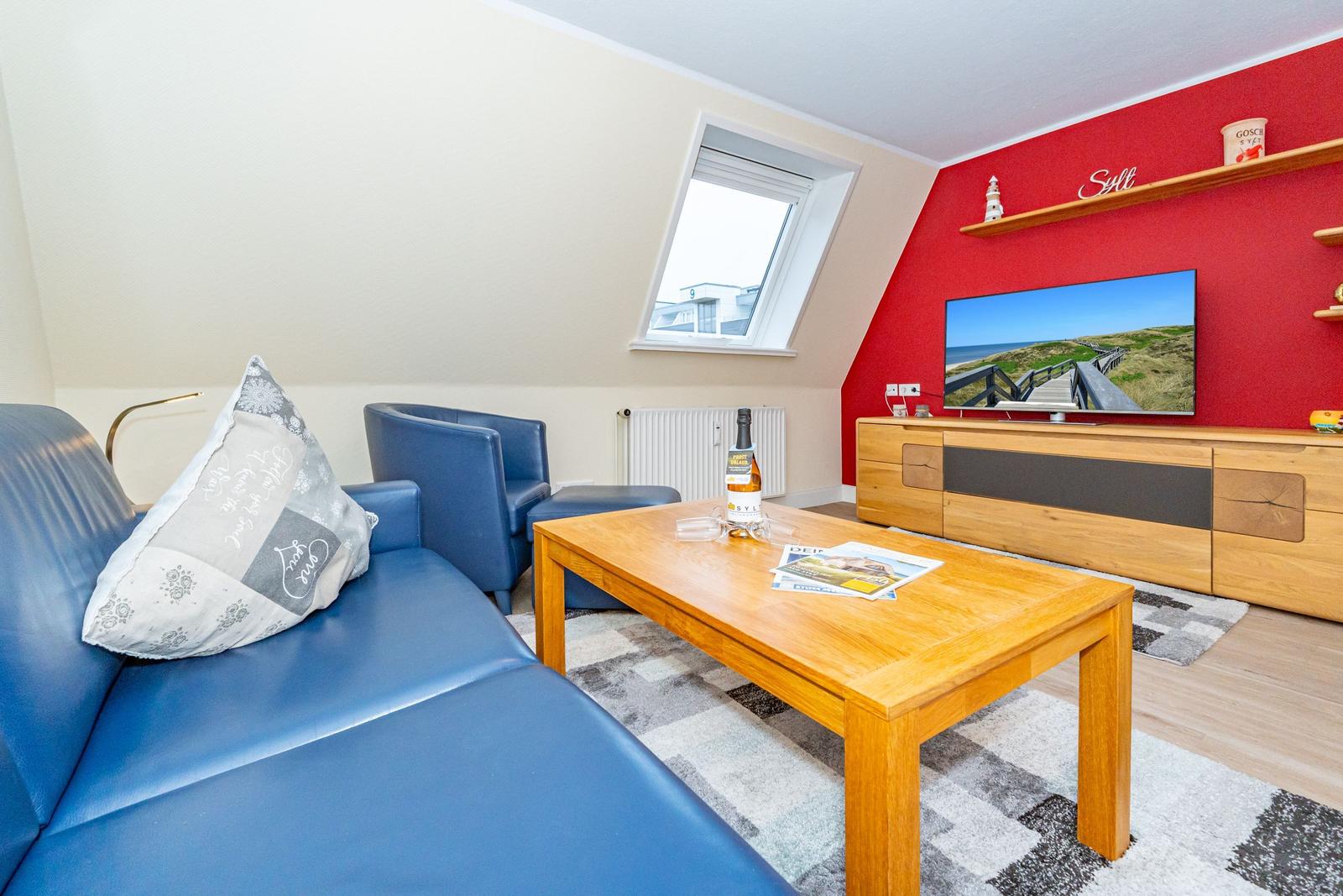 Wohnzimmer mit blauem Sofa, Holztisch und Fernseher an roter Wand.