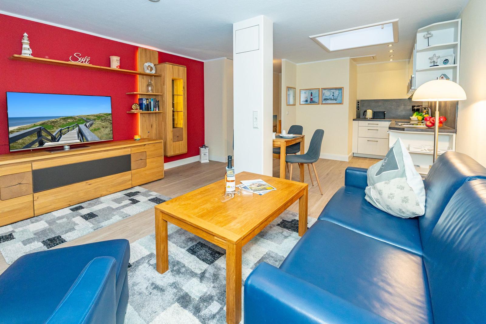Wohnzimmer mit blauem Sofa, Holztisch und Fernseher an roter Wand.