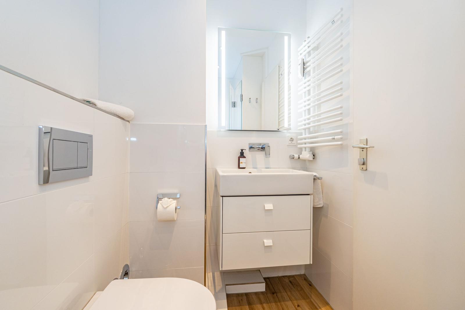 Badezimmer mit Waschbecken, Spiegel, Heizkörper und Toilette.