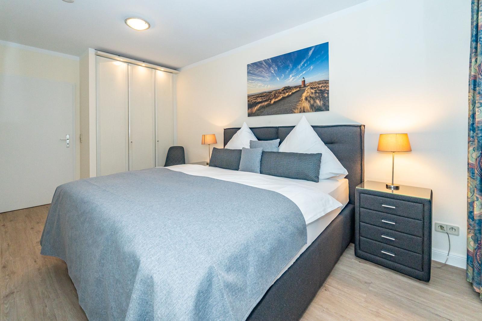 Schlafzimmer mit Doppelbett, Nachttisch und Kleiderschrank. Wandbild zeigt Leuchtturm.