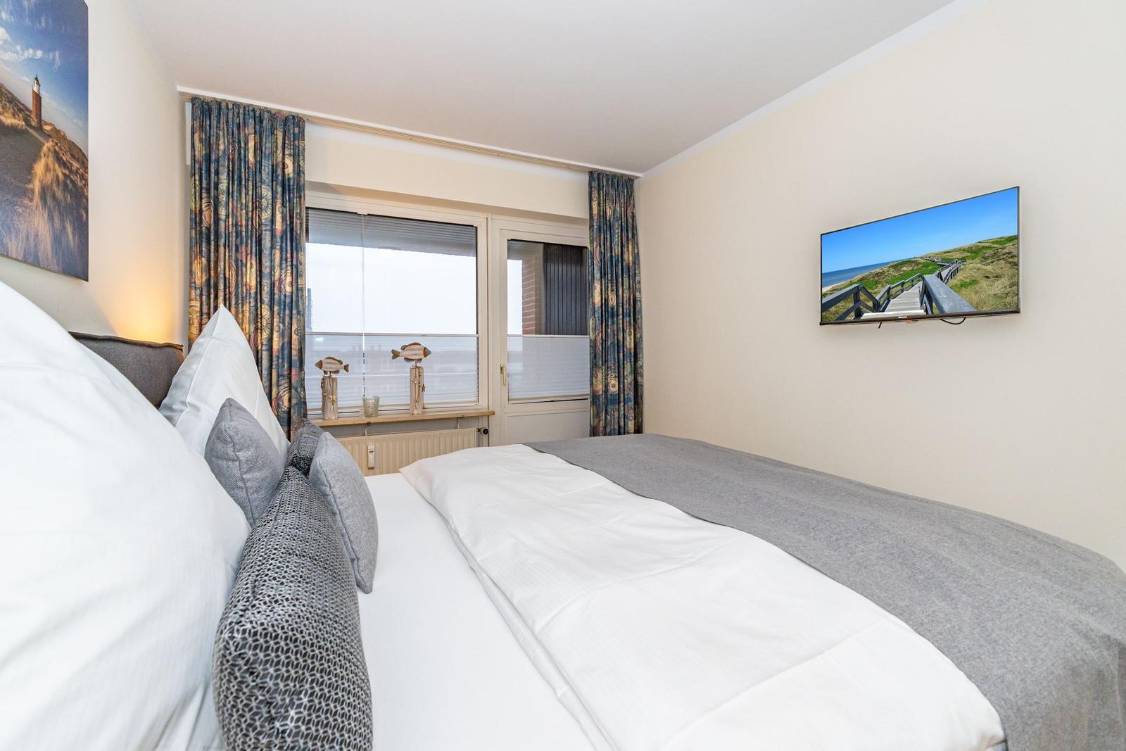 Schlafzimmer mit Bett, Fenster und Fernseher an der Wand.