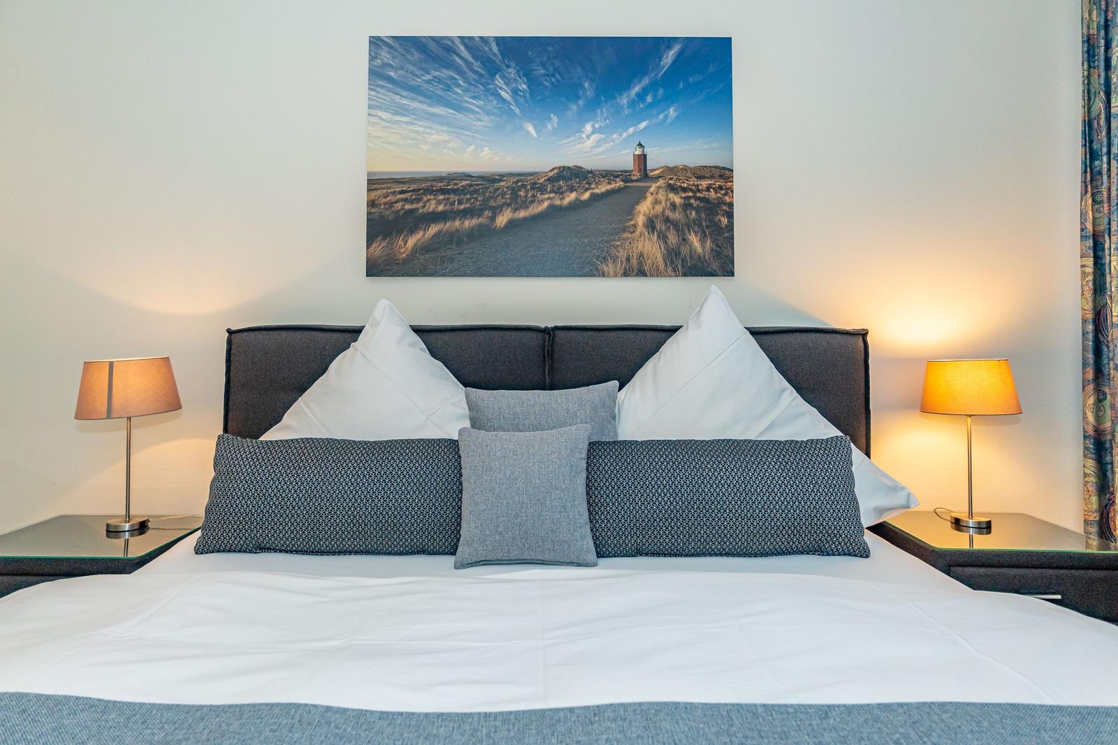 Schlafzimmer mit Bett, Kissen und Wandbild eines Leuchtturms.