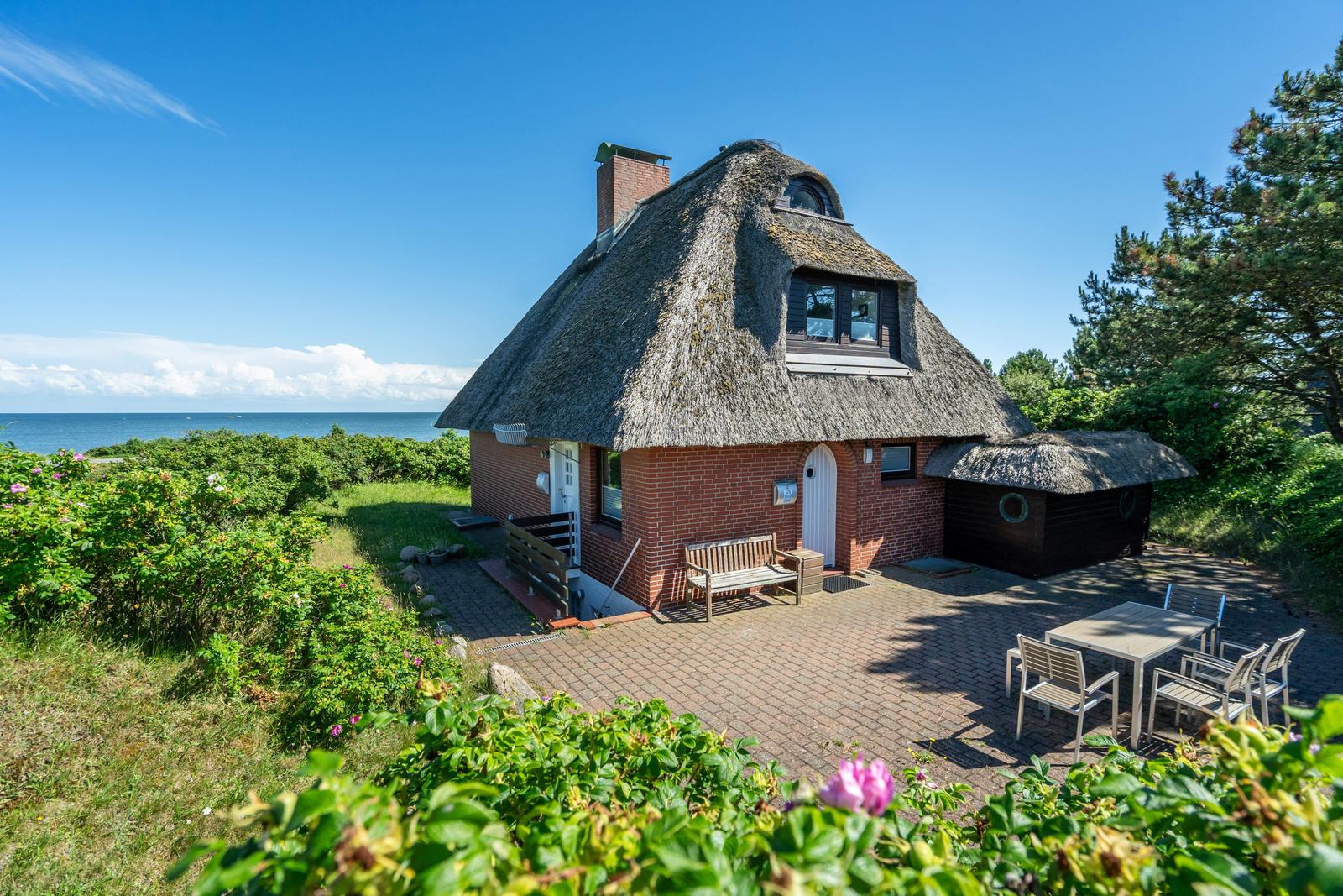 Haus mit Strohdach, Terrasse und Garten, Blick auf Meer und Himmel.