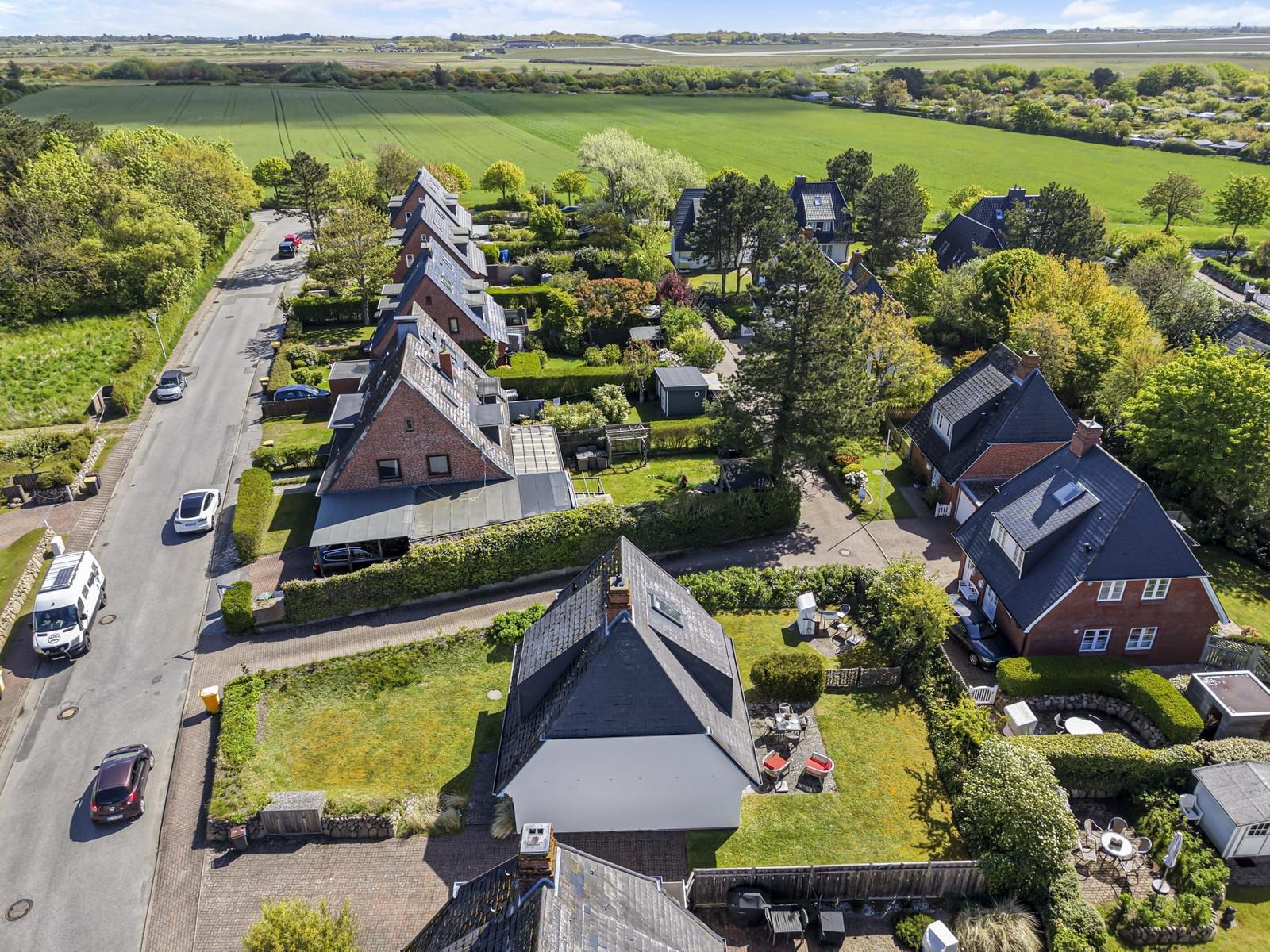 Aerial view of residential area with houses, gardens, and surrounding green fields.