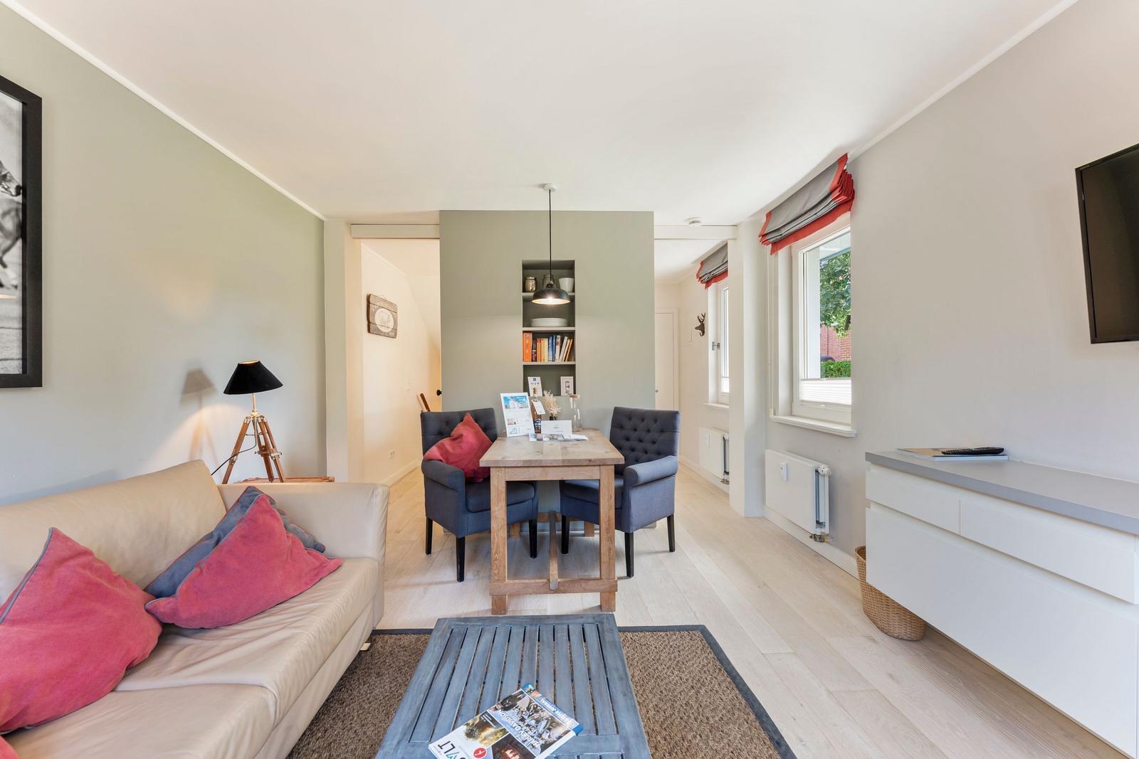 Living room with sofa, dining table, and window. Wooden floor and wall shelf visible.