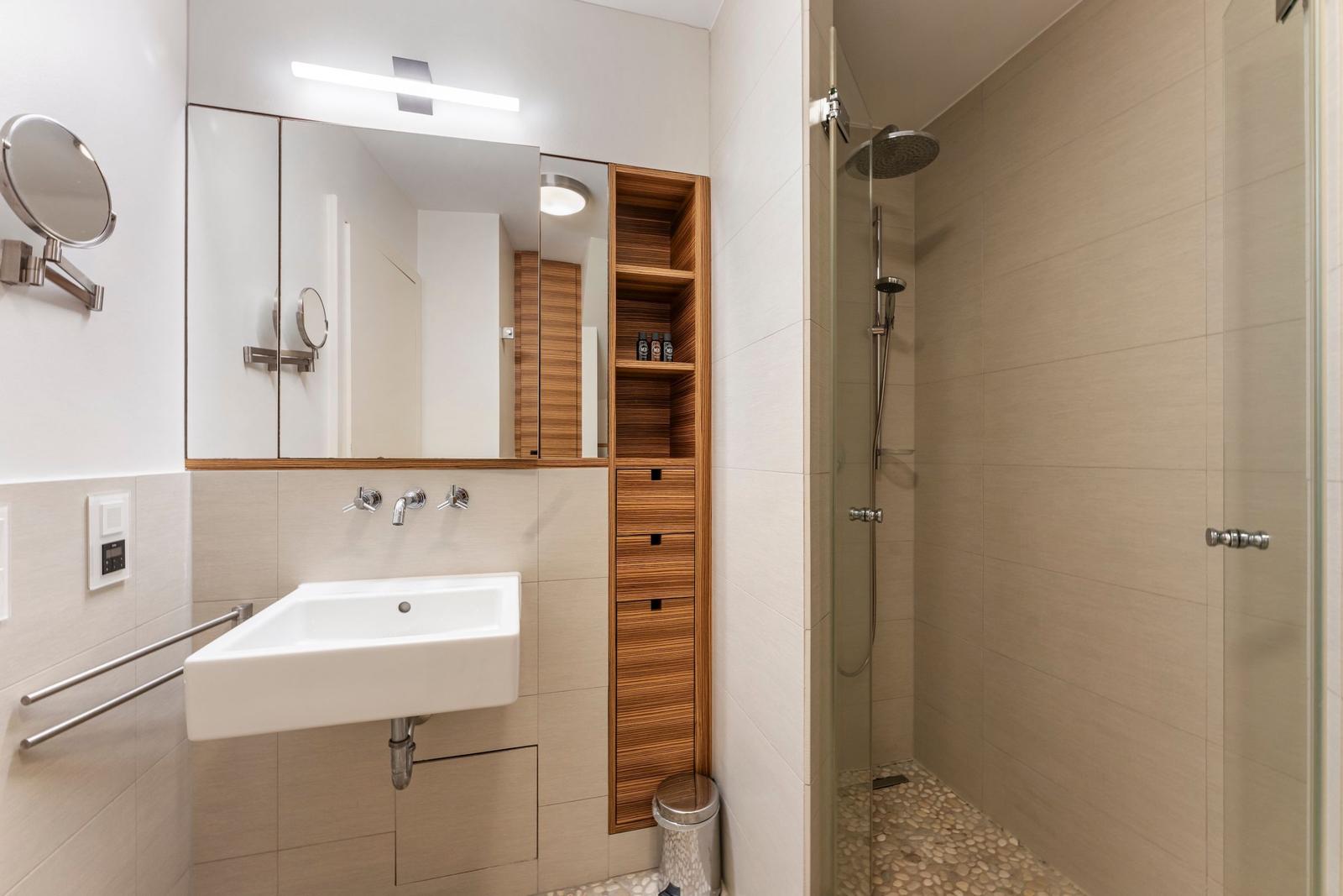 Bathroom with shower, sink, and wooden shelf.
