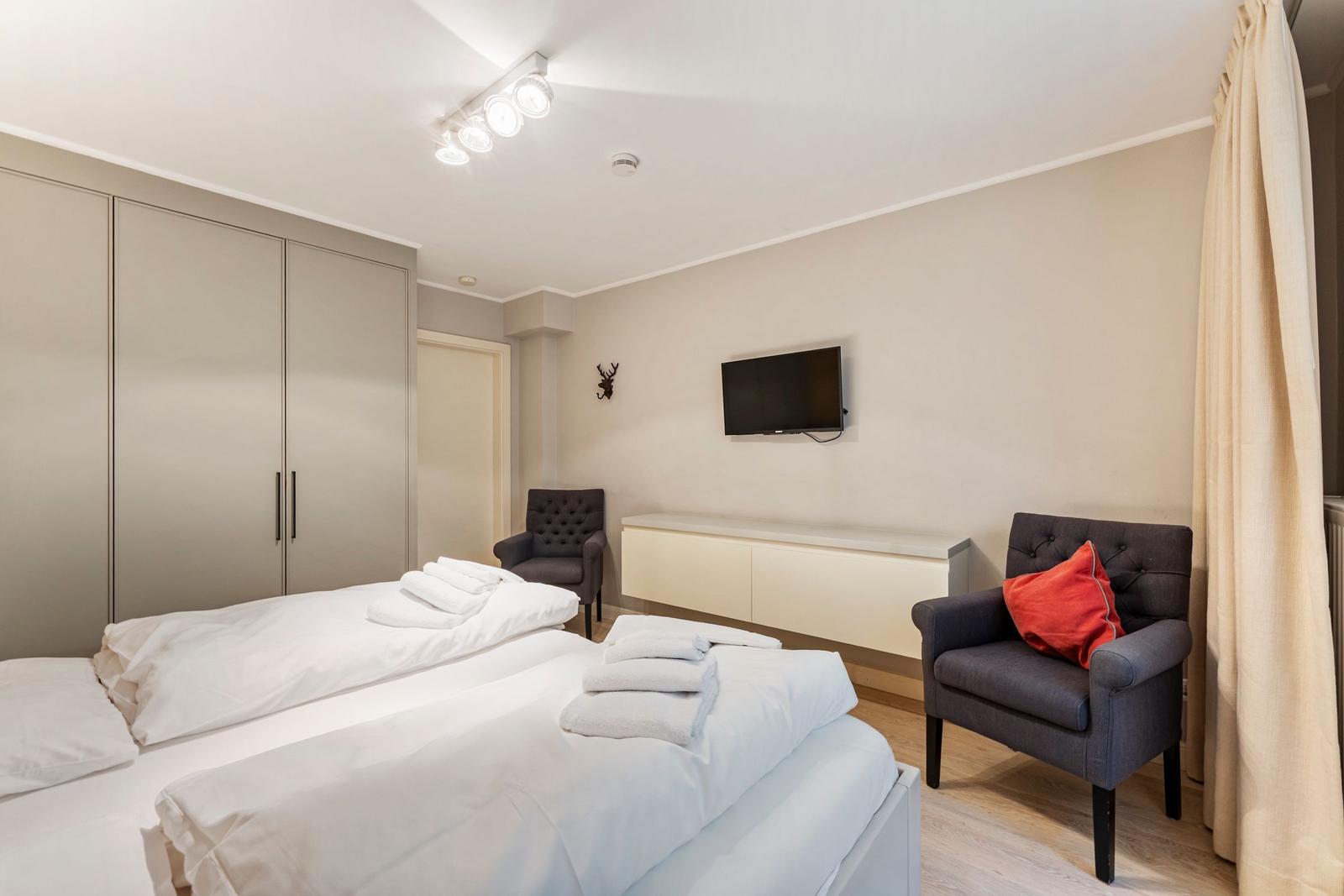 Bedroom with double bed, wardrobe, TV, and two armchairs.
