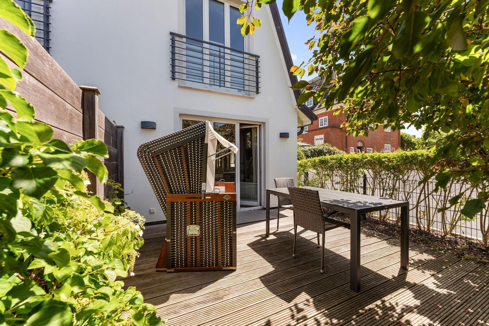 Terrace with table, chairs, and sunshade. Backyard with hedge and view of neighboring house.