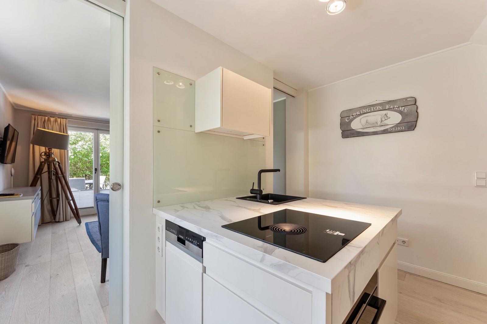 Kitchen with marble countertop, induction cooktop, and sink. Wall art and view into living area.