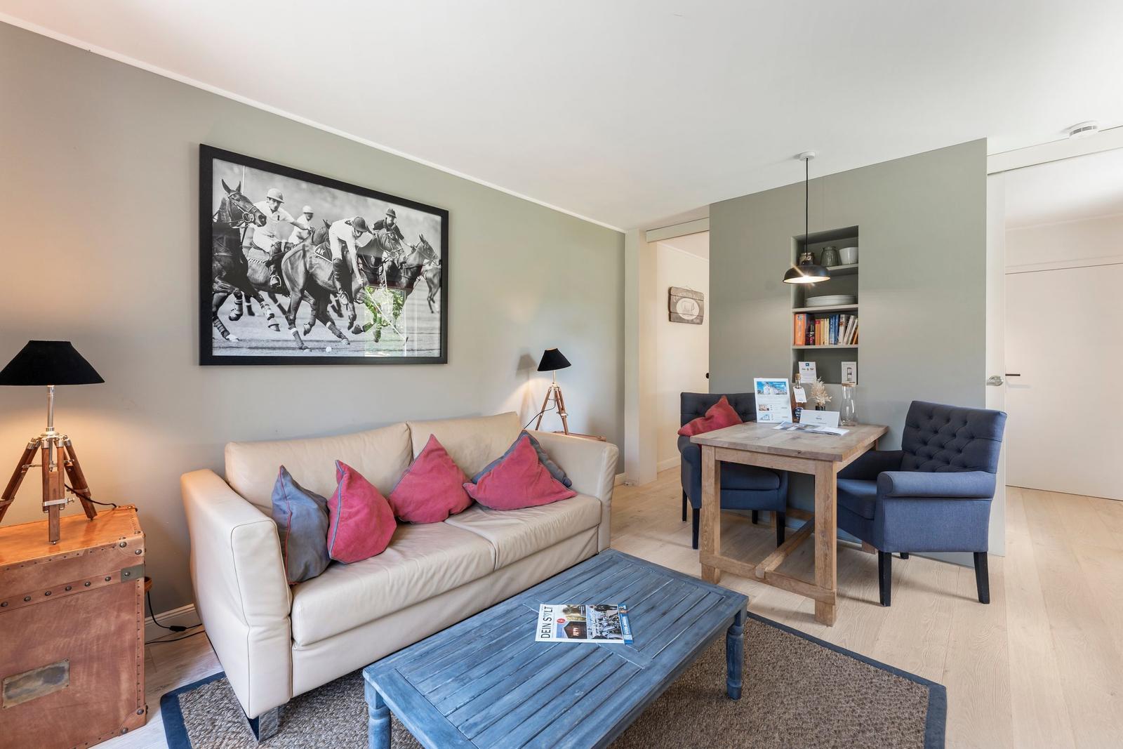 Living area with sofa, coffee table, and dining area. Wall art shows polo players.