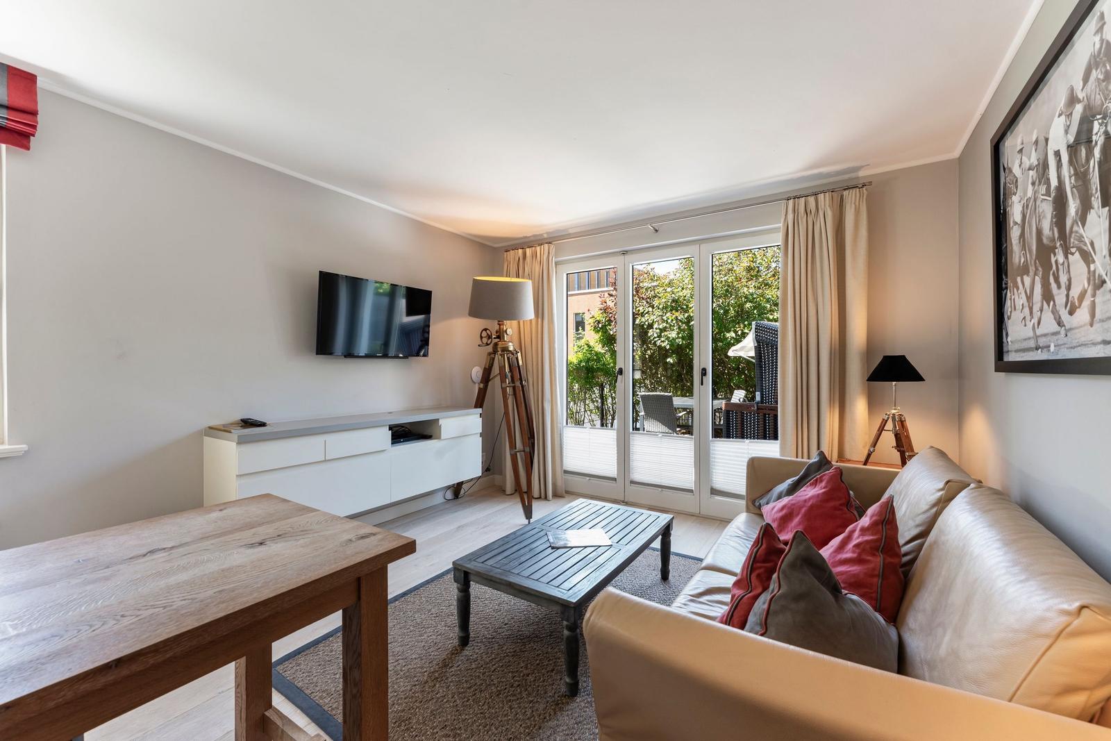 Living room with sofa, coffee table, and TV. Access to terrace with view of greenery.