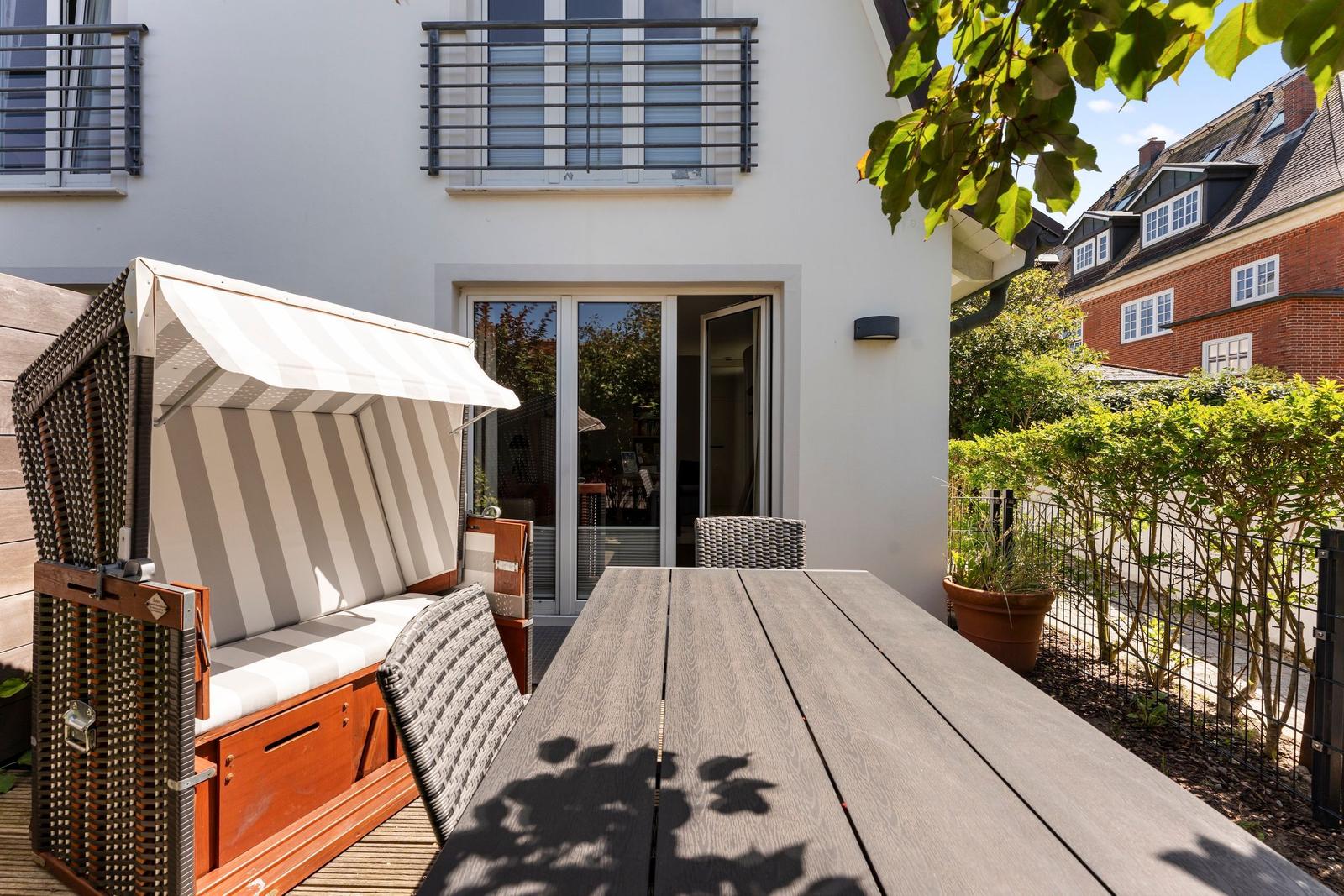 Terrace with wooden table, lounge chair, and glass doors to the apartment.