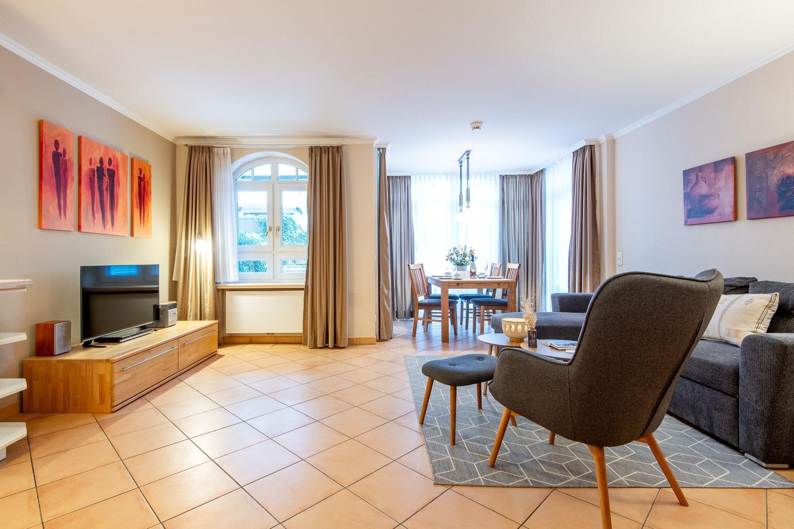 Wohnzimmer mit Sofa, Sessel, Fernseher und Essbereich mit Tisch und Stühlen.
