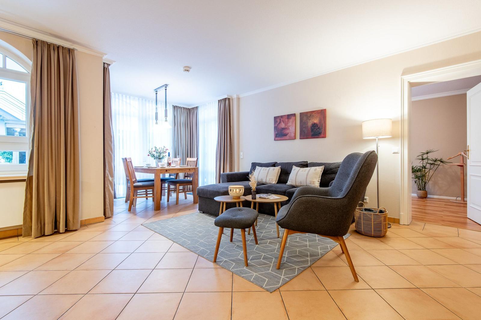 Wohnzimmer mit Sofa, Sessel und Esstisch. Fliesenboden und Wandbilder sichtbar.