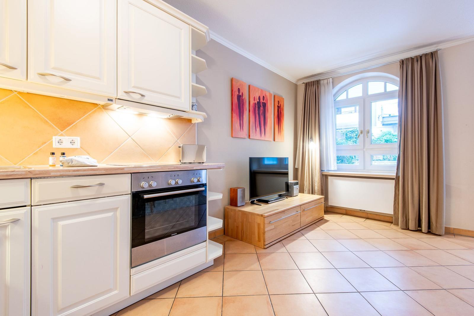 Küche mit weißen Schränken, Backofen und Fenster mit Vorhängen.