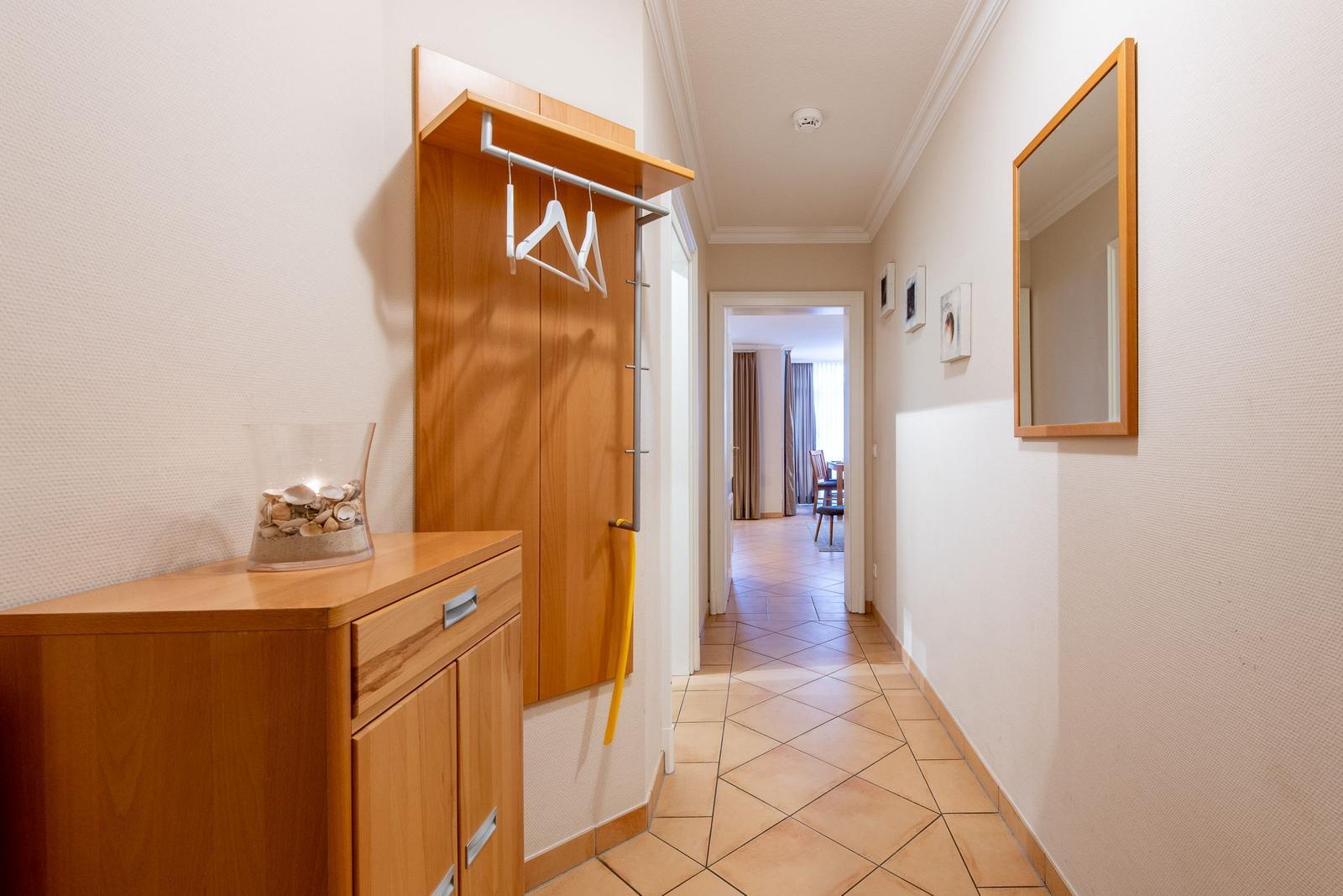 Flur mit Holzgarderobe, Spiegel und Vitrine mit Muscheln.