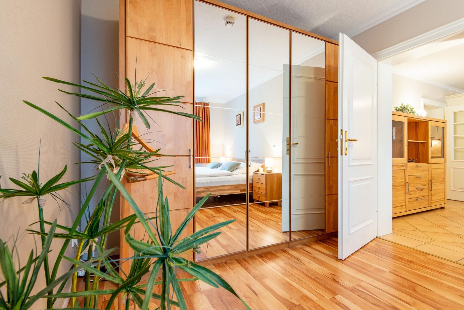 Schlafzimmer mit Spiegelschrank, Holzboden und Pflanze im Vordergrund.