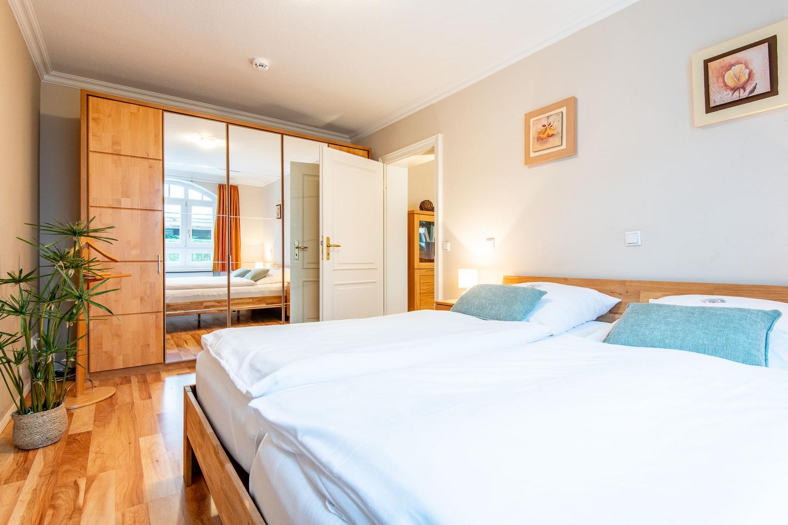 Schlafzimmer mit Doppelbett, Holzmöbel und Spiegelschrank. Holzfußboden und Pflanze.