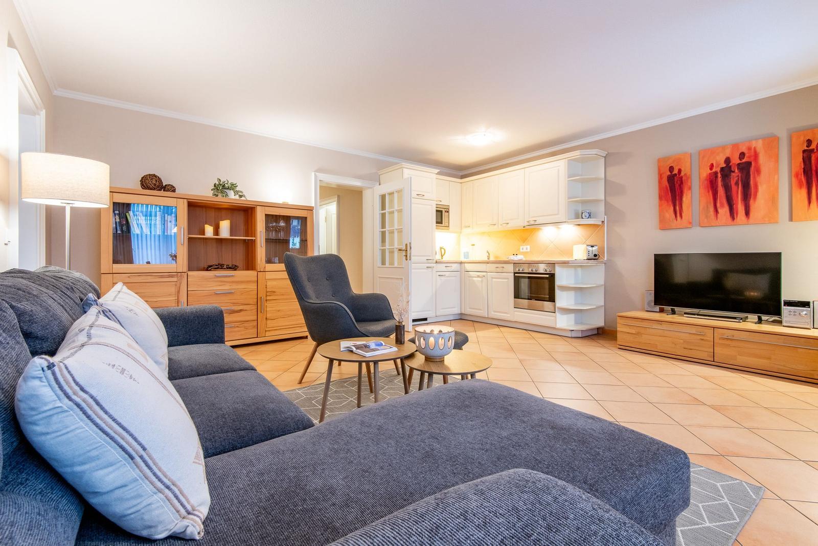 Wohnzimmer mit Sofa, Sessel, Küchenbereich und Fernseher.