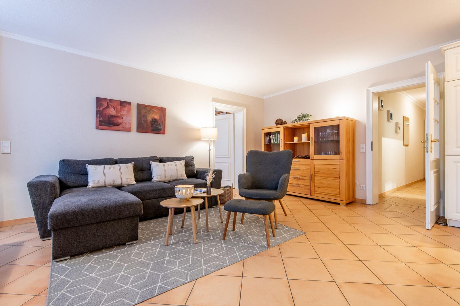 Wohnzimmer mit Sofa, Sessel, Couchtisch und Holzschrank.