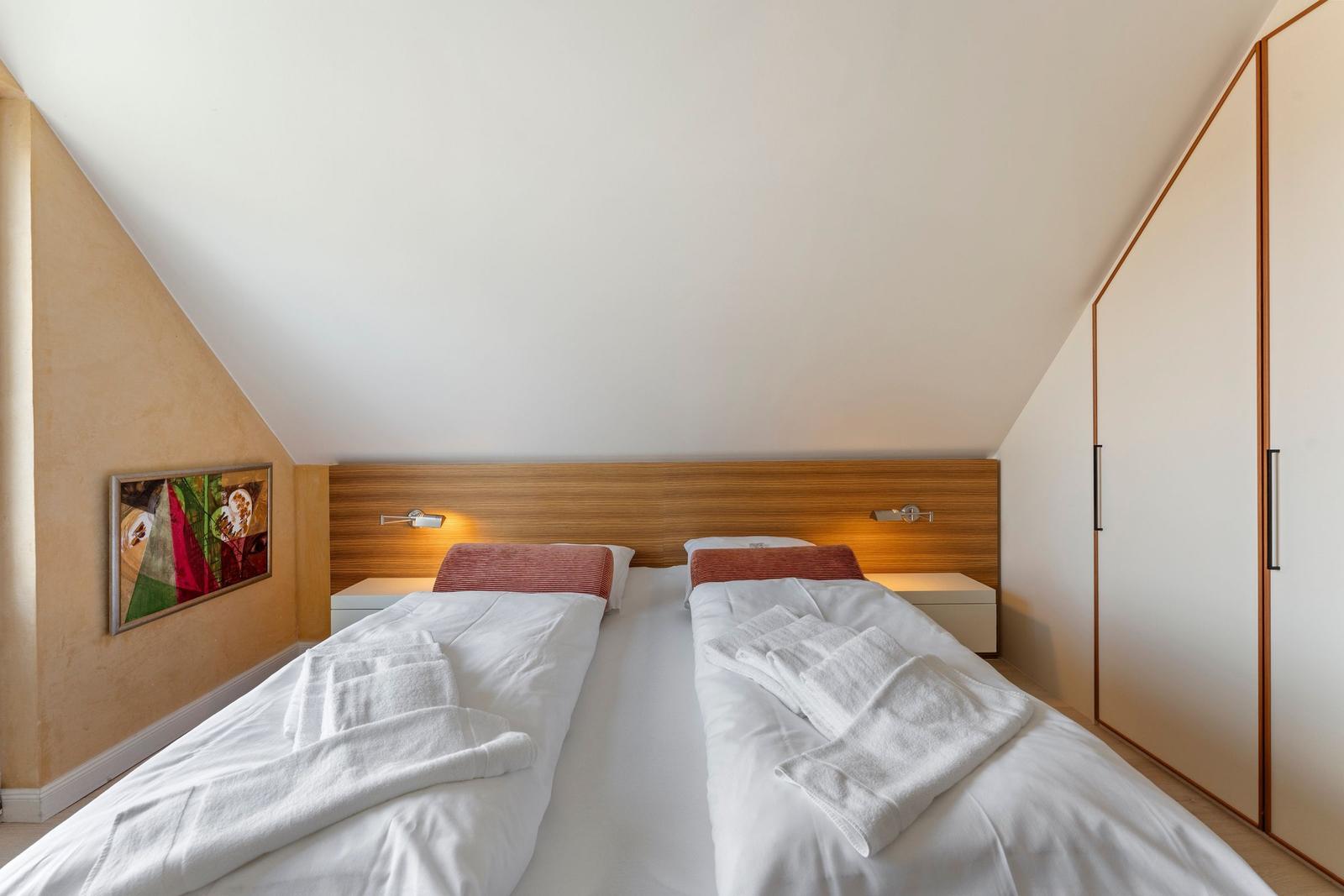 Zimmer mit Doppelbett, Holz-Kopfteil, Nachttischen und Kleiderschrank unter schrägem Dach.