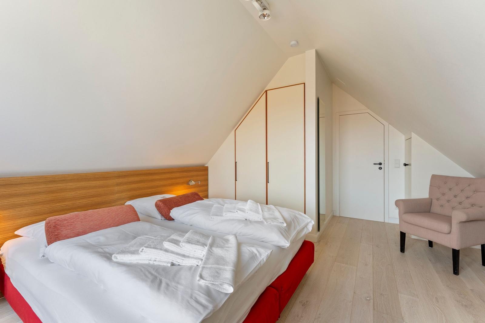 Schlafzimmer mit Doppelbett, Kleiderschrank und Sessel unter Dachschrägen.