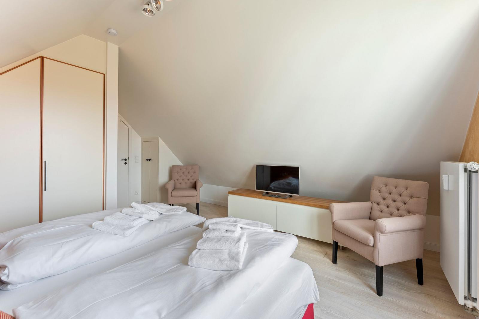 Schlafzimmer mit Doppelbett, zwei Sesseln, Fernseher und Kleiderschrank.