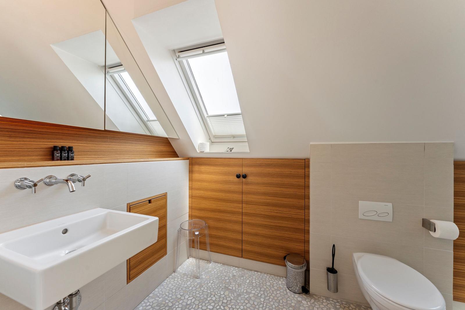 Badezimmer mit Dachfenster, Waschbecken, Toilette und Holzverkleidung.
