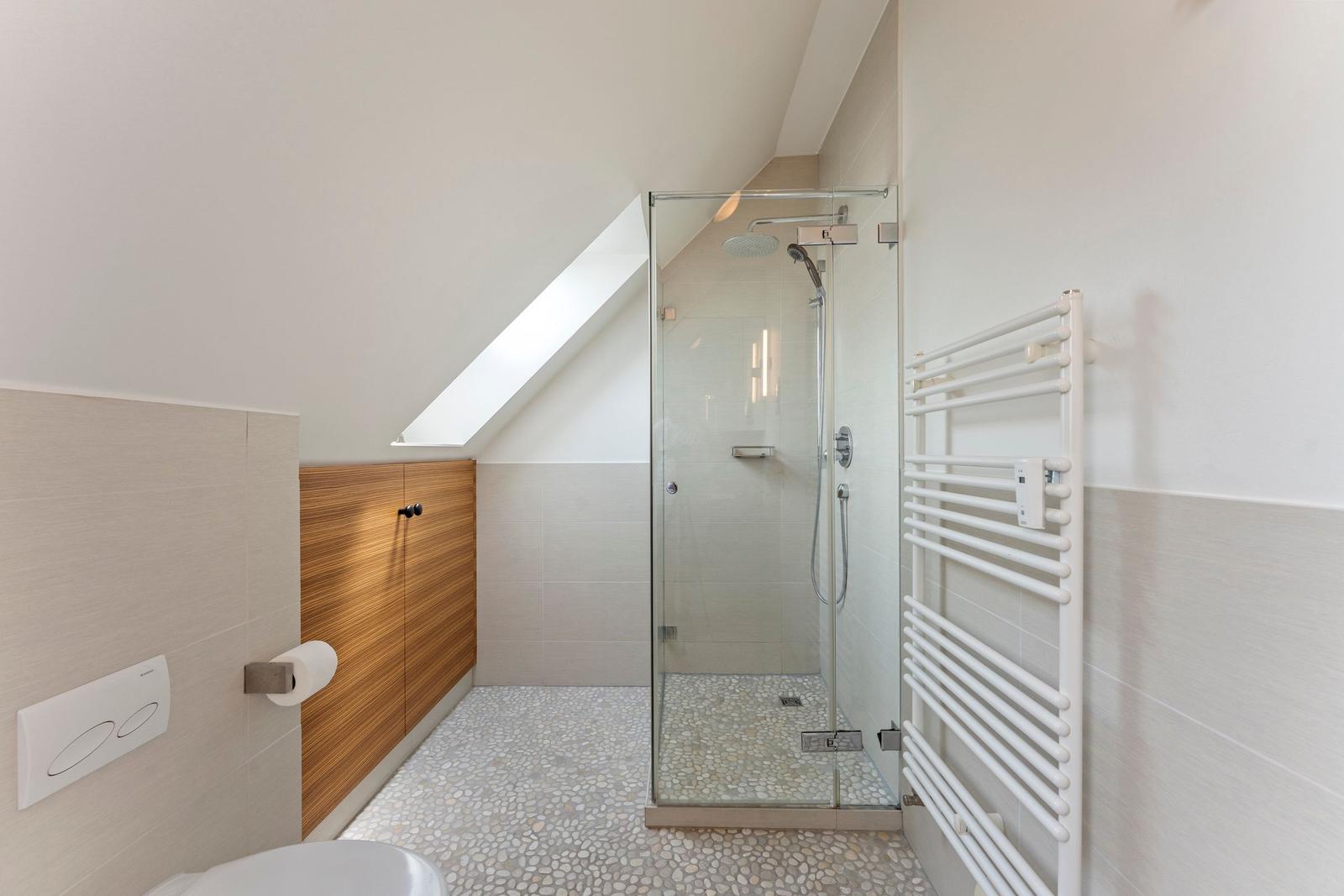 Badezimmer mit Dusche, Heizkörper und Holzschränken unter Dachschrägen.