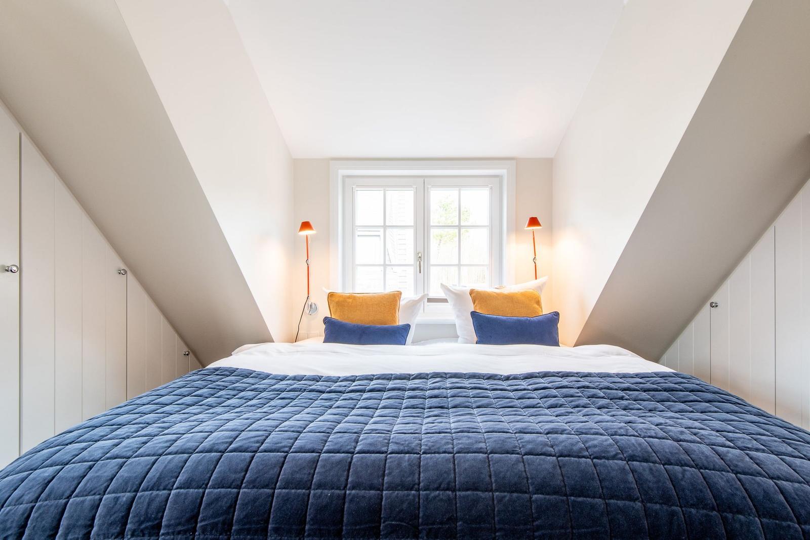 Schlafzimmer mit Dachschrägen, großem Bett und Fenster.