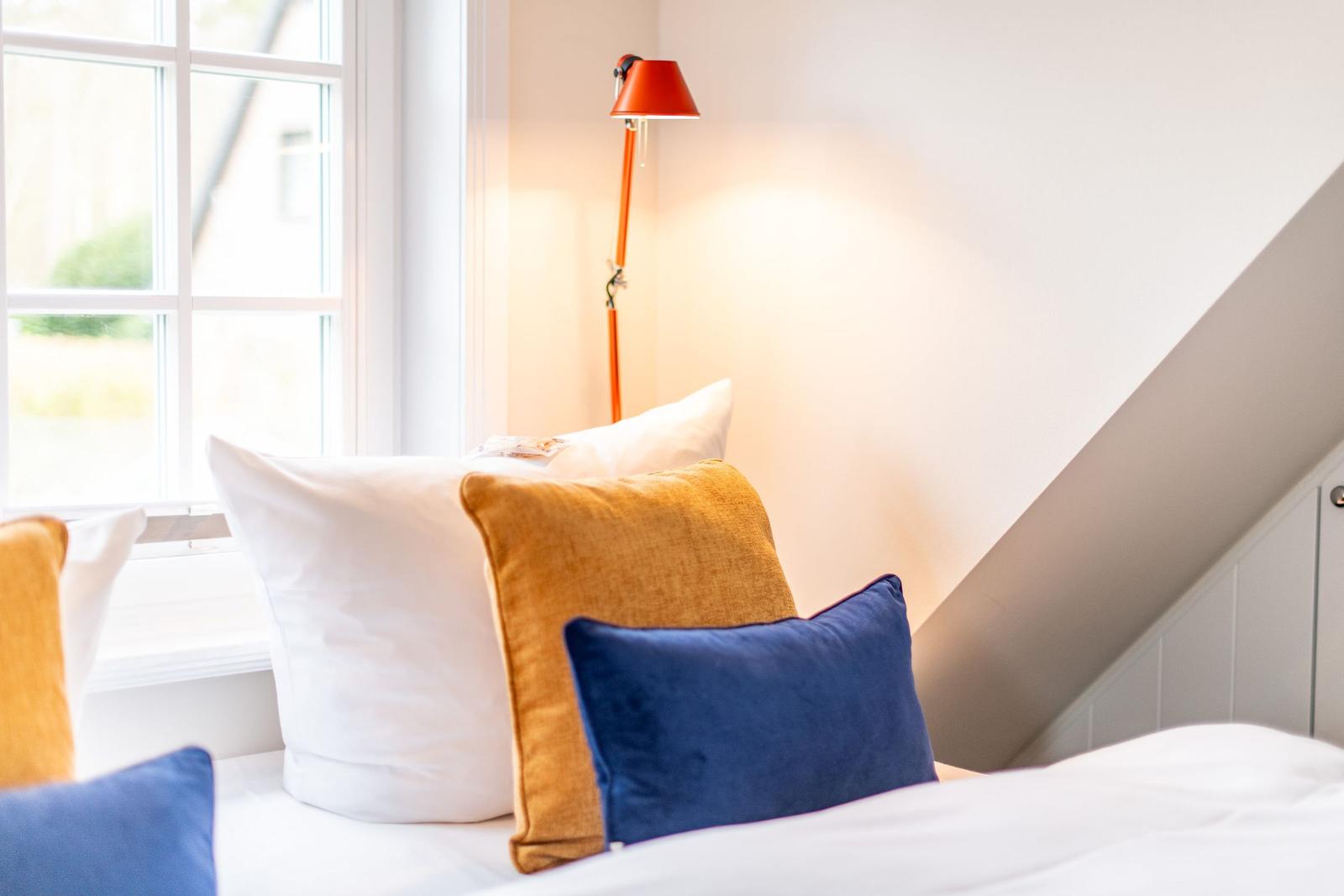 Ein Bett mit Kissen und einer Stehlampe neben einem Fenster.